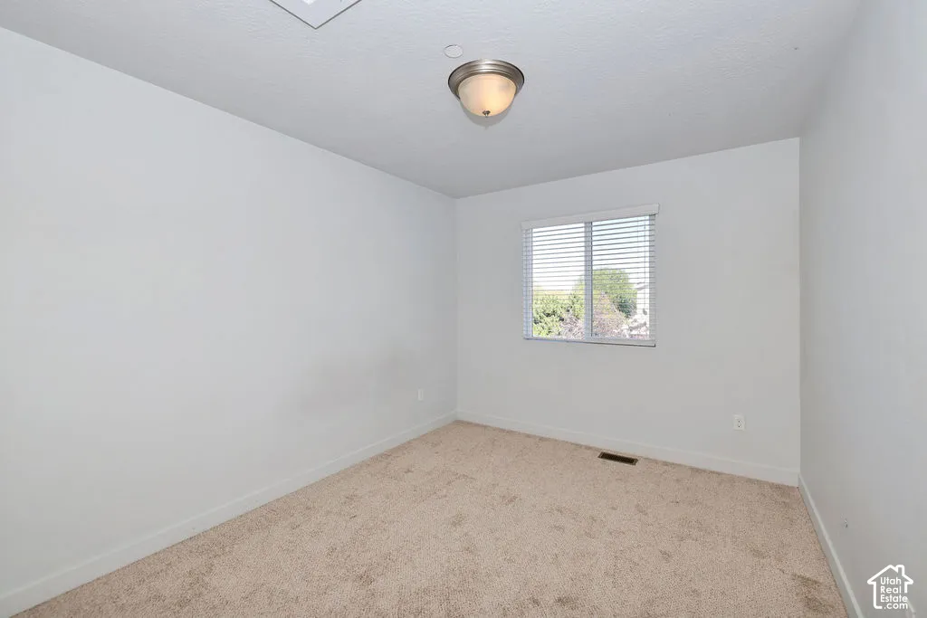 Neutral interior space featuring wall-to-wall carpeting, a window with horizontal blinds, and a semi-flush mount ceiling light fixture