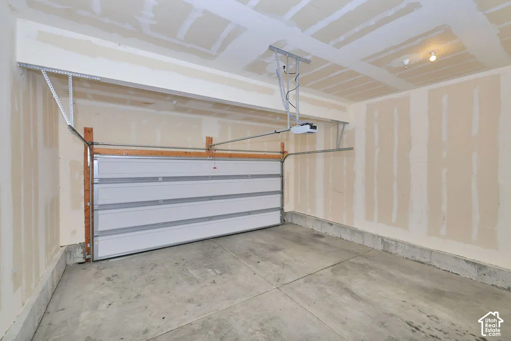 Attached garage with a white sectional overhead door, concrete flooring, automatic garage door opener, and unfinished drywall walls