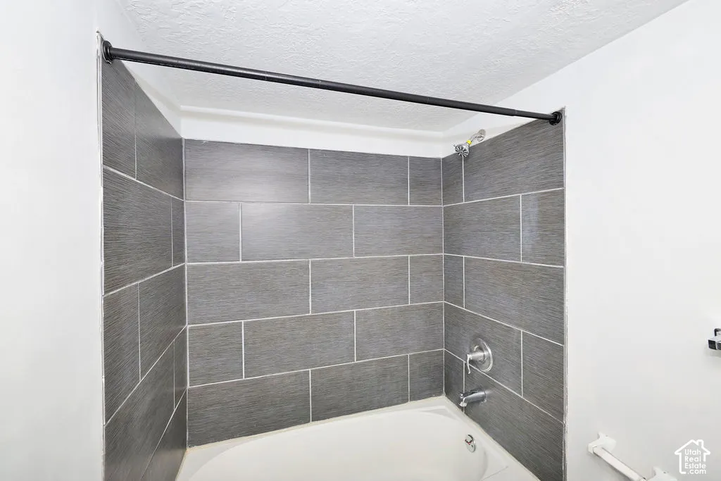 Shower alcove featuring large-format dark gray wall tiling, a built-in tub, and chrome hardware
