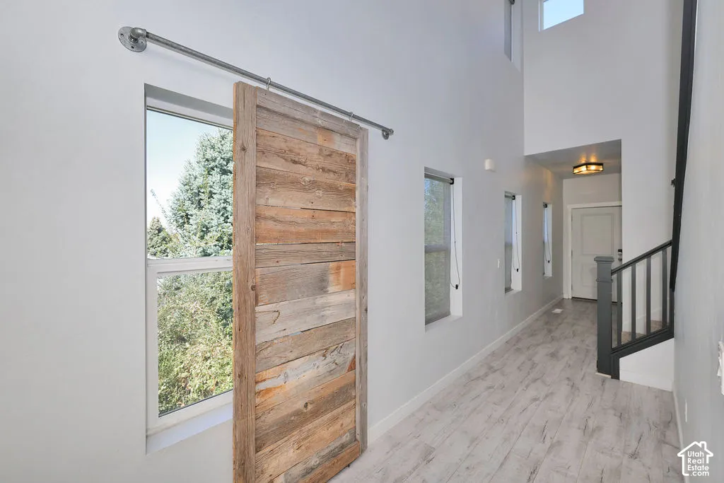 High-ceiling entryway featuring wood-finish flooring, a rustic sliding barn door on a metal track, multi-paneled windows, and a staircase with a dark-finished railing