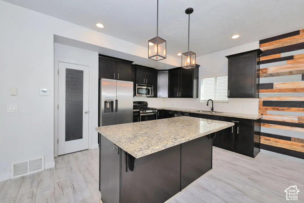 Kitchen featuring dark cabinetry, stone countertops, a center island, wood-finish flooring, and a decorative wood-plank accent wall