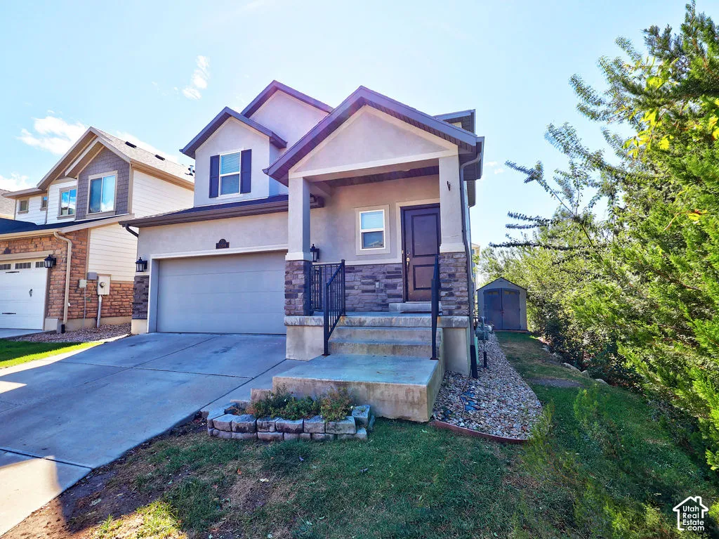 Two-story exterior featuring a stucco and stone facade, attached two-car garage, covered entryway with metal railing, and concrete driveway