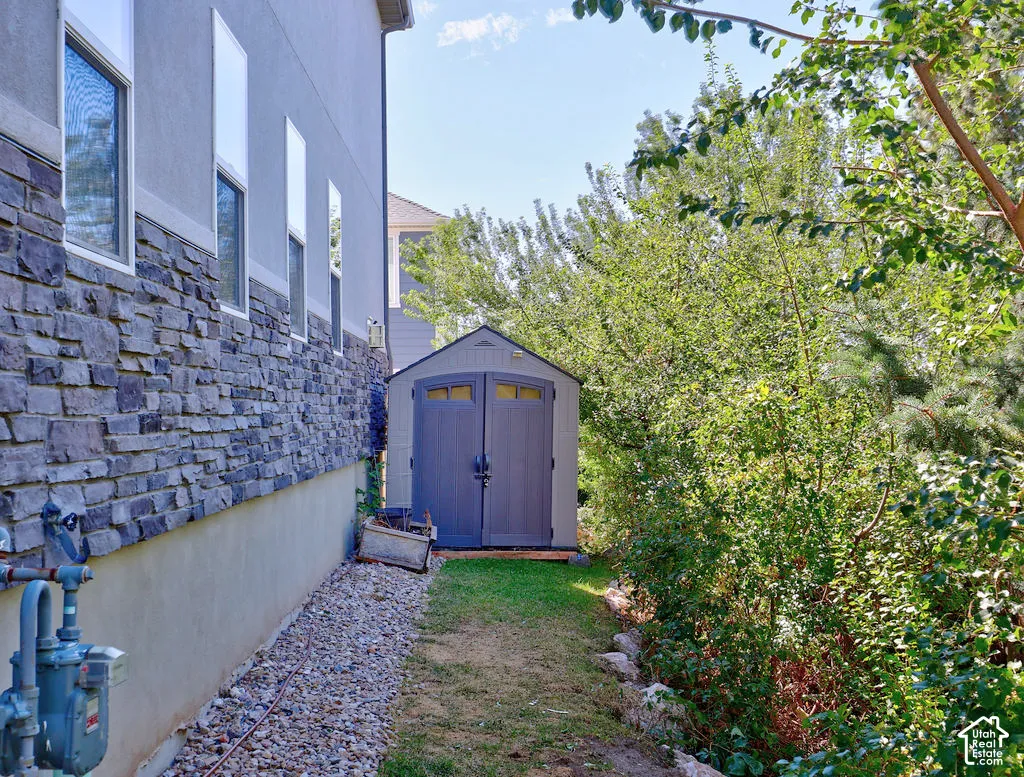 Exterior side yard featuring stone veneer siding, gravel ground cover, and a detached storage structure