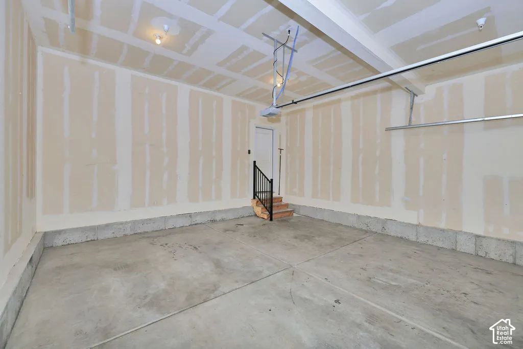Garage space featuring concrete flooring, unfinished drywall, a motorized overhead door opener, and a single-door entry with a black metal handrail