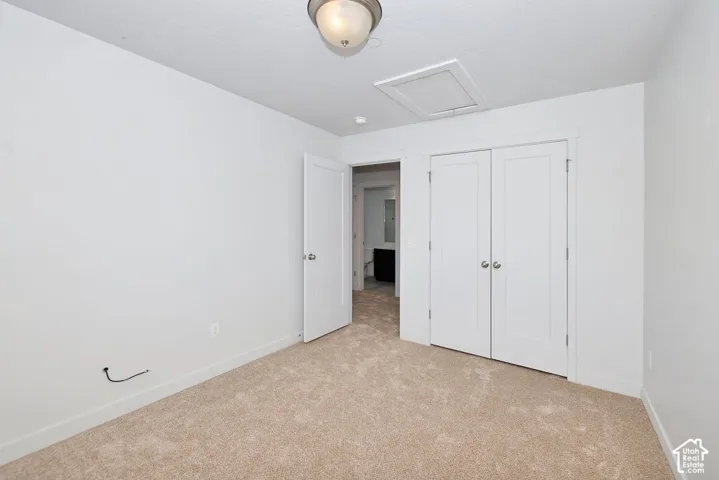 Neutral-toned wall paint, light-colored carpet flooring, ceiling-mounted light fixture, white interior doors, and a closet with bifold doors