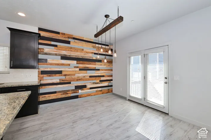 Reclaimed wood accent wall, wood-finish flooring, built-in kitchen cabinetry with light-toned countertops, contemporary chandelier, and double patio doors