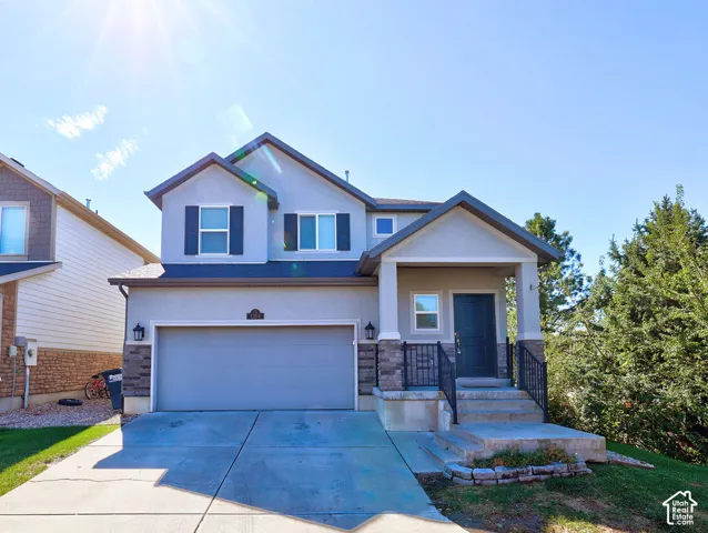 Two-story exterior with a covered entry, attached garage, stone accents, and a concrete driveway