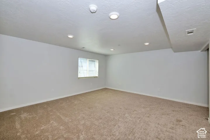 Neutral-toned carpet flooring, recessed ceiling lighting, textured white walls, and a window with horizontal blinds