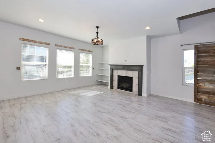 Light wood-finish flooring, a fireplace with tile surround and dark mantel, a wood-slat barn door, and a decorative ceiling light fixture