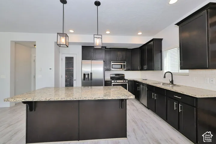Spacious kitchen featuring dark cabinetry, stainless steel appliances, light-toned countertops, and a full tile backsplash