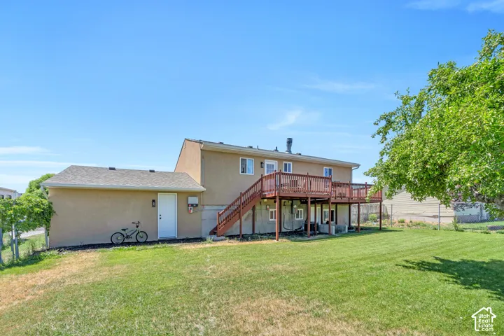 Expansive backyard featuring a manicured lawn, stucco exterior, and a multi-level wood deck with stairs