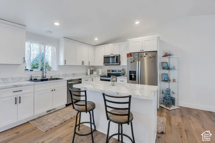 White cabinetry, stainless steel appliances, marble-finish countertops, central island, and wood-finish flooring