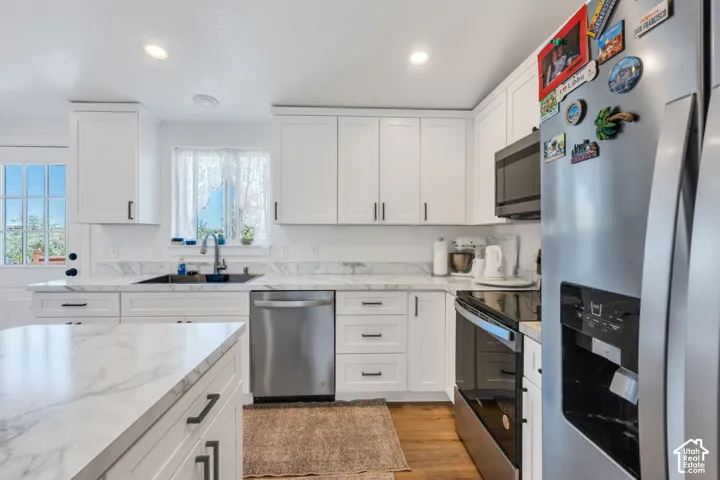 White shaker cabinetry with dark hardware, stainless steel appliances, marbled countertops, recessed lighting, and wood-finish flooring