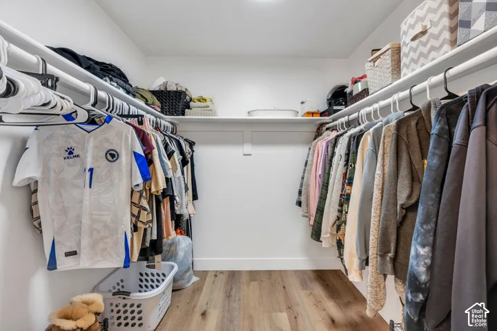 Walk-in closet featuring wood-finish flooring, white walls, and built-in shelving with hanging rods