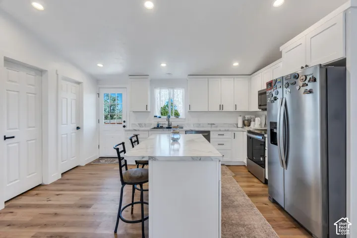 Open-concept kitchen featuring wood-finish flooring, a central island with a stone-finish countertop, white cabinetry, and stainless steel appliances