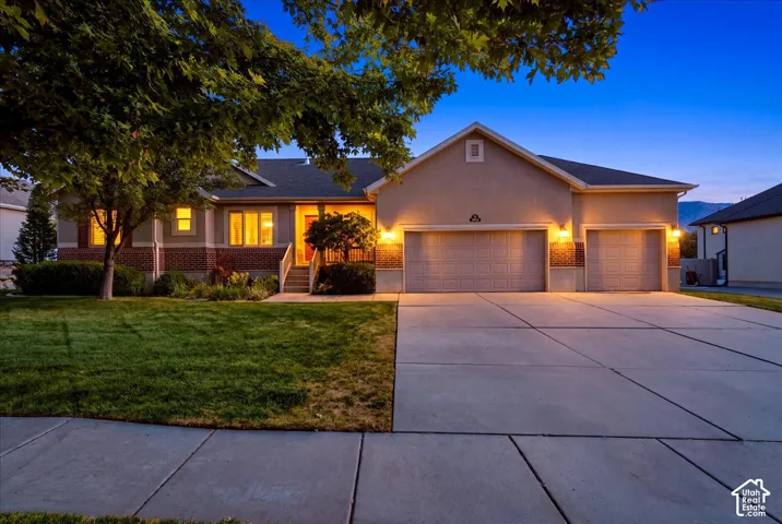 Stucco exterior with brick accents, attached multi-car garage, concrete driveway, front porch, and mature landscaping
