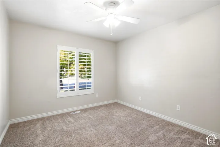 Window with plantation shutters, ceiling fan with integrated lighting, neutral-toned walls, and carpeting