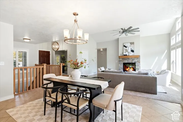 Open-concept living space featuring vaulted ceilings, a stone-faced fireplace with wood mantel, multiple windows, and a ceiling fan