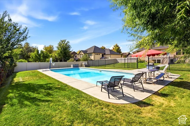 Expansive backyard featuring a rectangular swimming pool, concrete pool deck, and surrounding lawn with mature trees