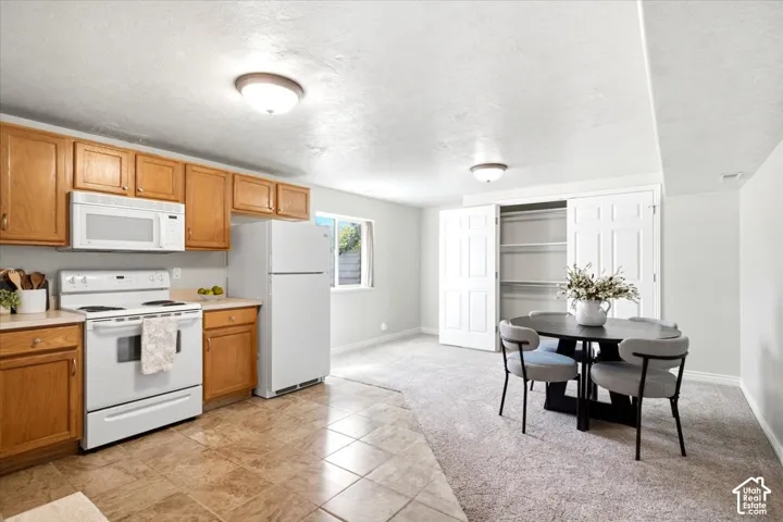 Kitchen with wood cabinetry, tile flooring, and white appliances including an oven, microwave, and refrigerator