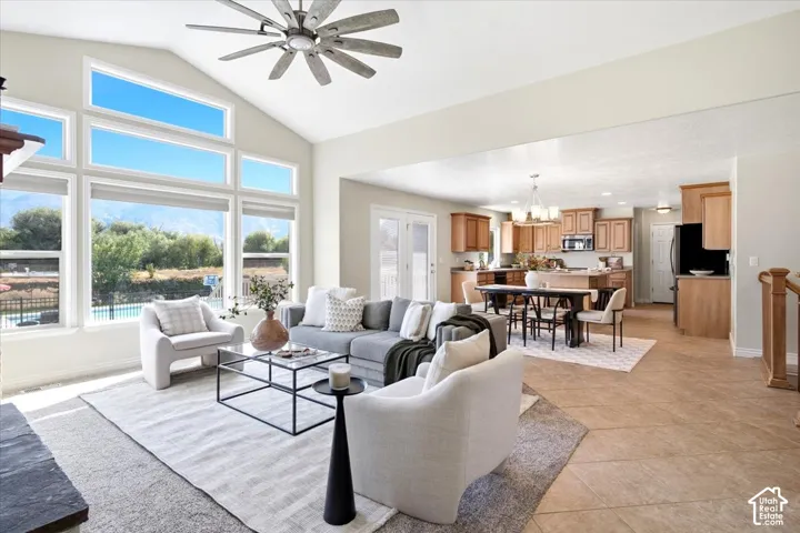 Vaulted ceiling with ceiling fan, large windows with mountain and pool scenery, open-concept living space, wood-finish cabinetry, and tiled flooring