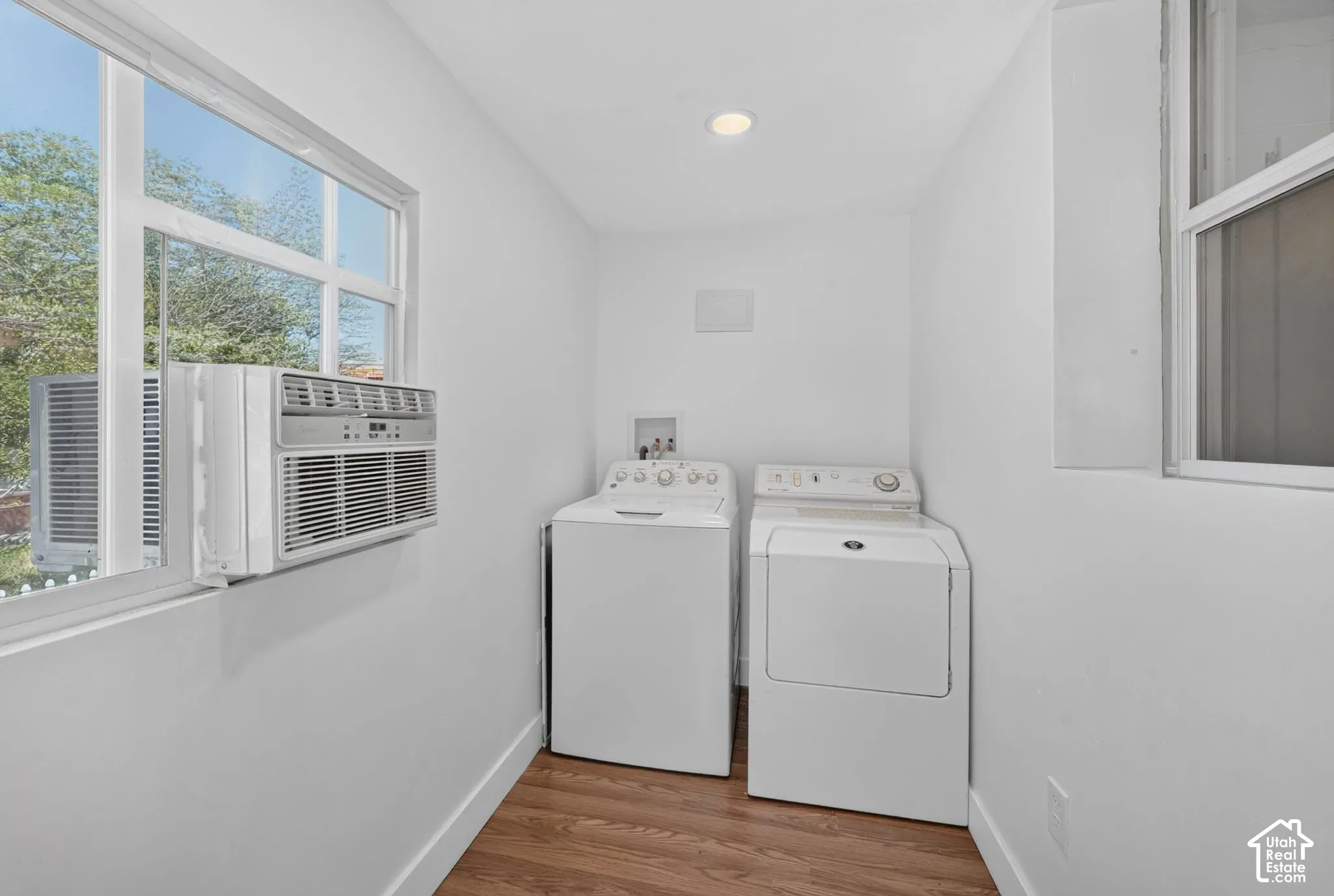 Laundry area with wood-finish flooring, recessed ceiling light, and window-mounted air conditioning unit