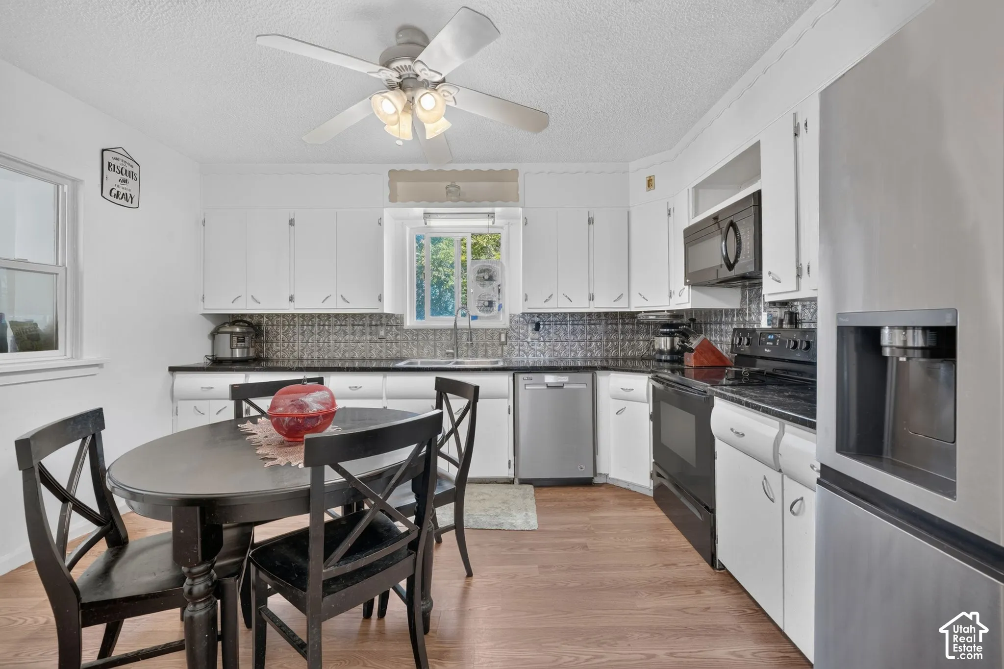 White cabinetry, dark countertops, tile backsplash, and stainless steel appliances
