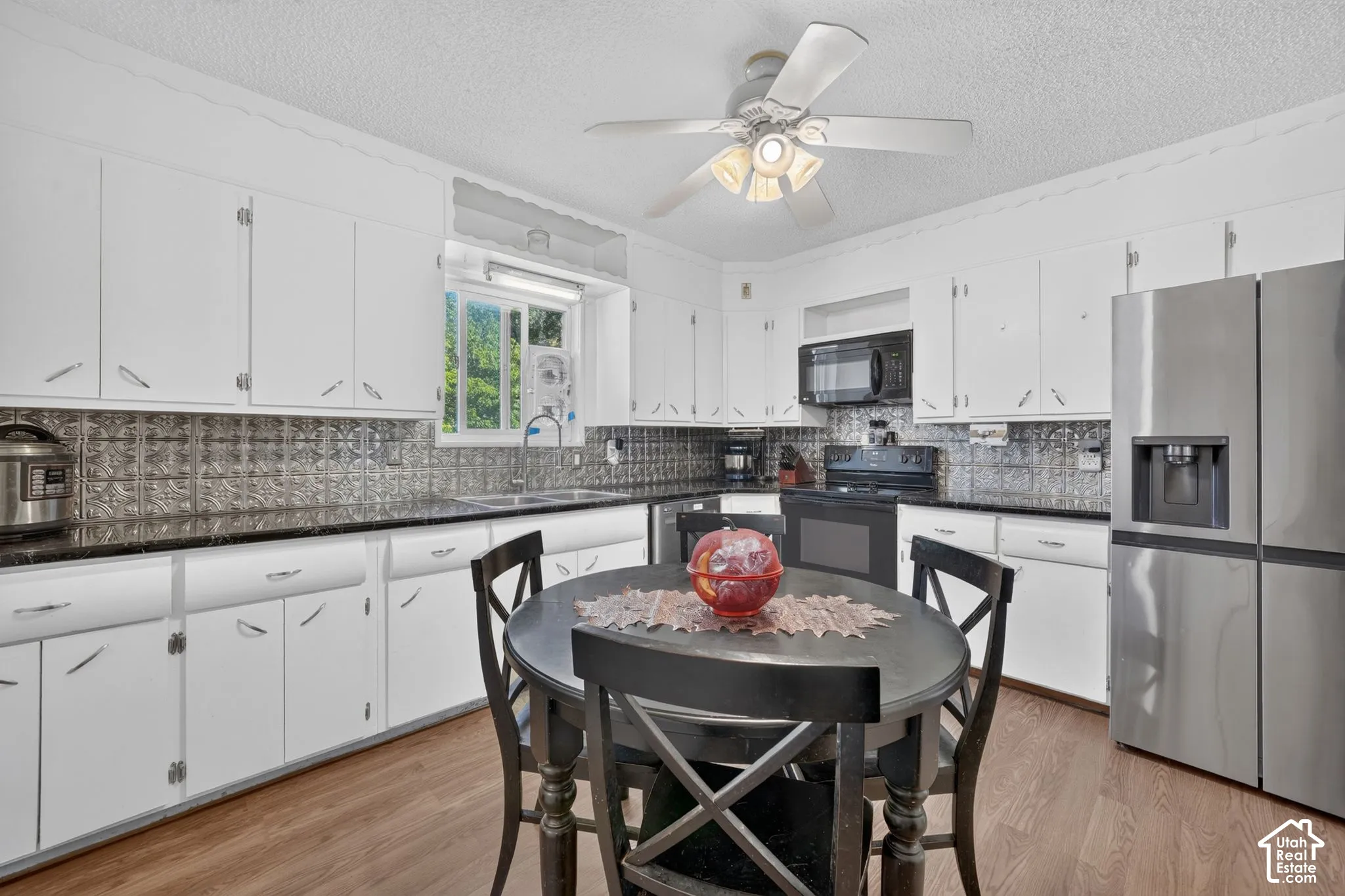 White cabinetry with chrome hardware, dark countertops, patterned tile backsplash, stainless steel refrigerator, and wood-finish flooring