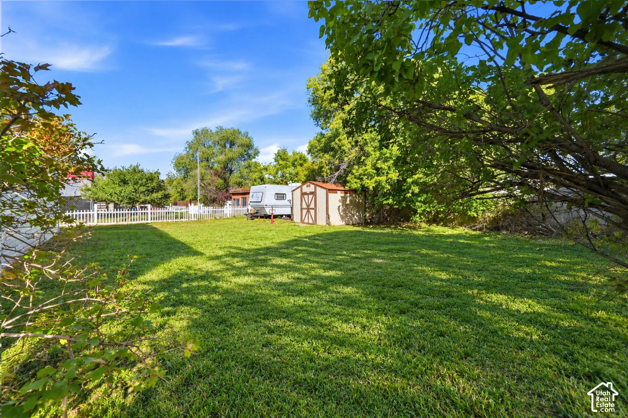 Expansive lawn space with mature trees and a white picket fence