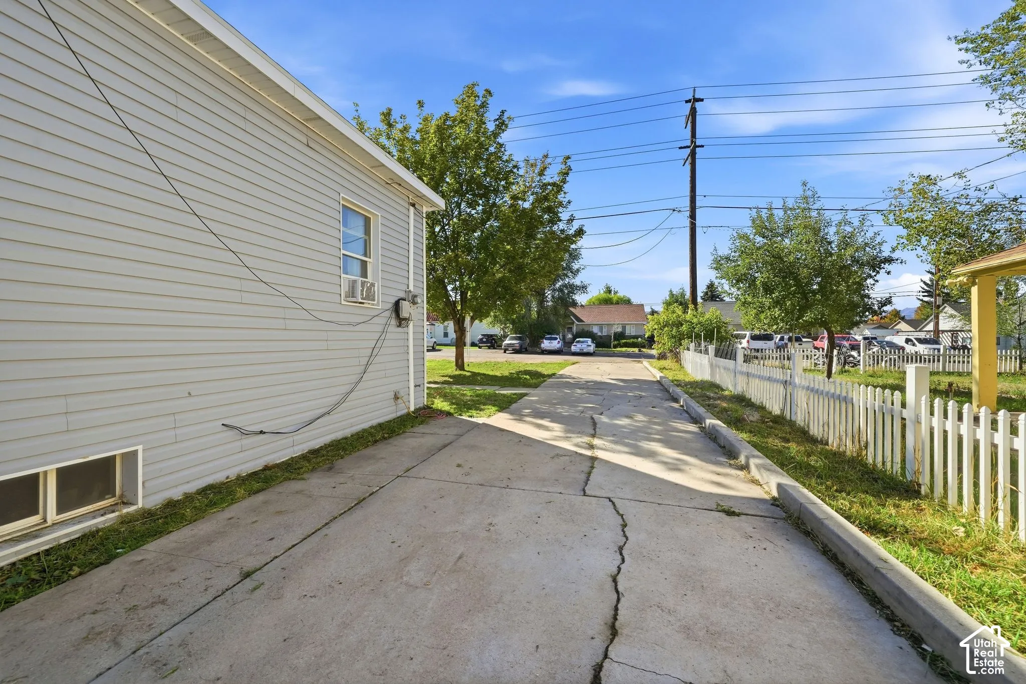 Concrete driveway with curbing, framed by a white picket fence and a gray siding exterior