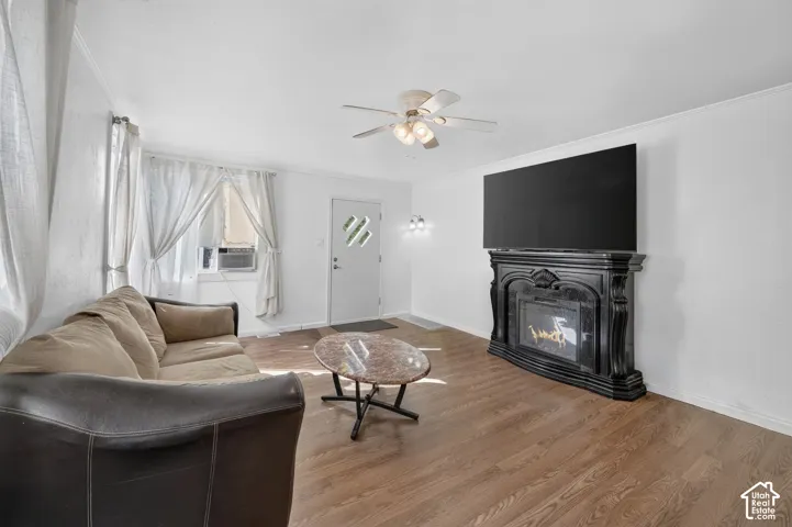 Wood-finish flooring, white walls, decorative fireplace, ceiling fan, and white entry door with decorative glass inserts