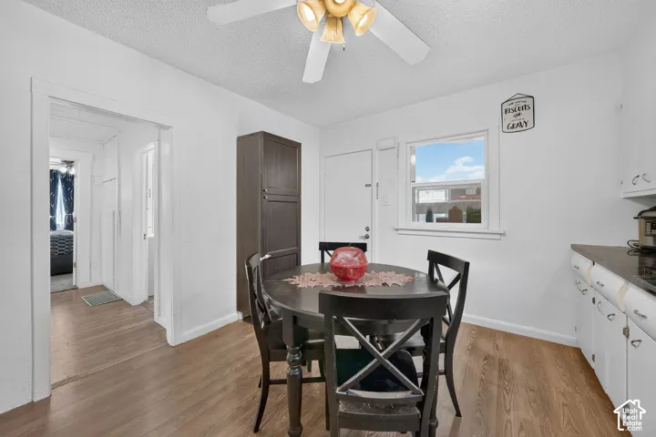 Wood-finish flooring, white walls, built-in dark wood storage cabinet, and a ceiling fan with integrated lighting