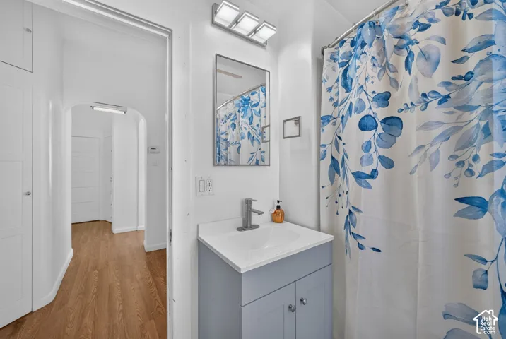 Bathroom featuring a single vanity with a light gray cabinet and white countertop, undermount sink with a chrome faucet, and a wall-mounted mirror with a three-light fixture