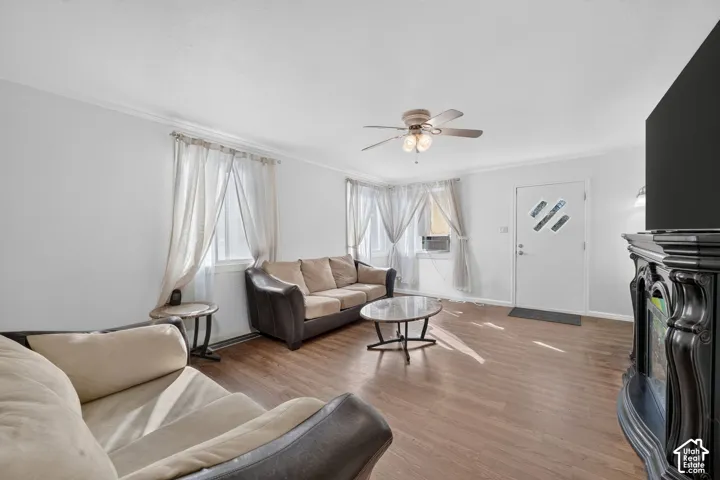 Wood-finish flooring throughout, a ceiling fan with integrated lighting, and multiple windows with crown molding