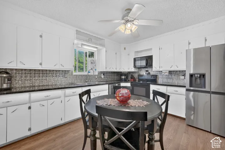 White cabinetry with chrome hardware, dark countertops, patterned tile backsplash, stainless steel refrigerator, and wood-finish flooring
