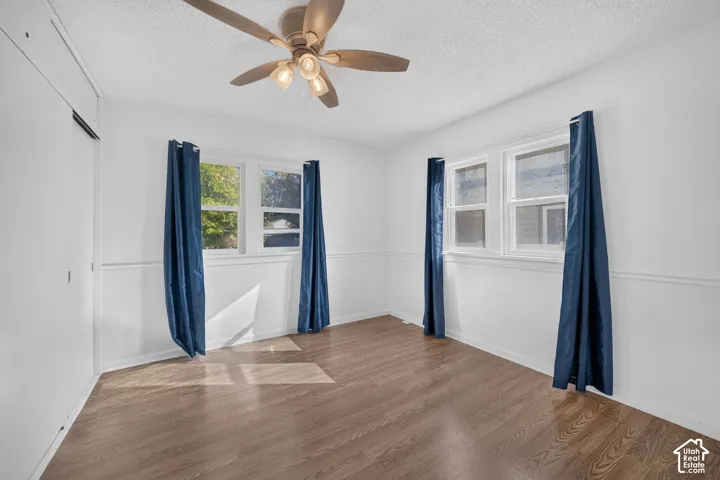Wood-finish flooring, two large windows, white paneled walls, and a ceiling fan with integrated lighting