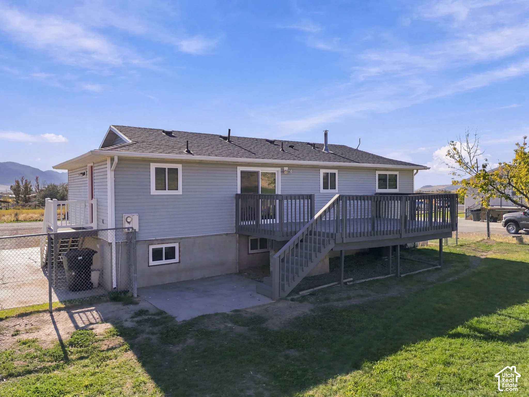 Rear exterior with an elevated wood-finish deck, concrete patio, and light-colored siding
