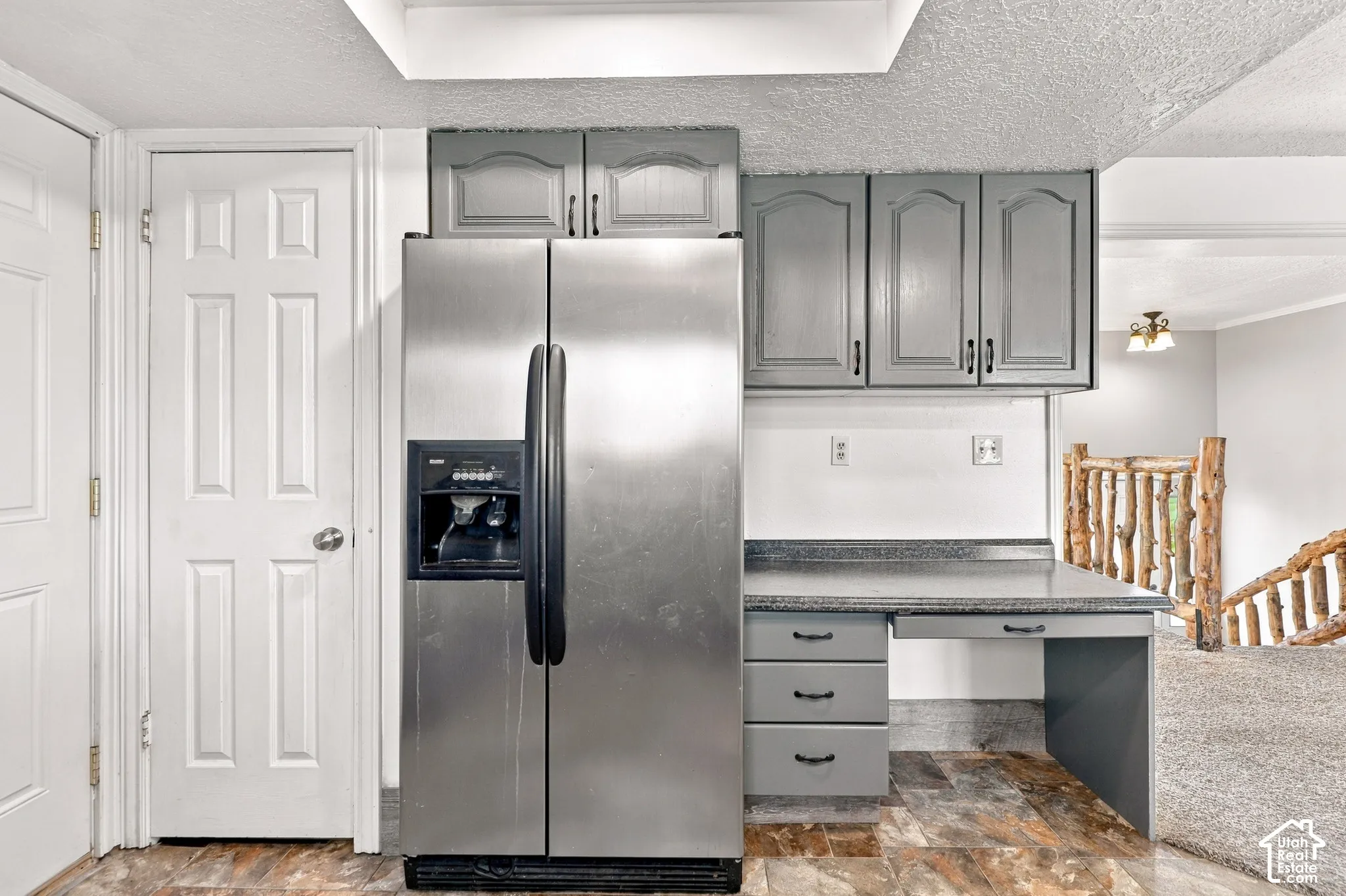 Stainless steel refrigerator, gray cabinetry, built-in desk, wood-finish flooring, and natural wood staircase railing
