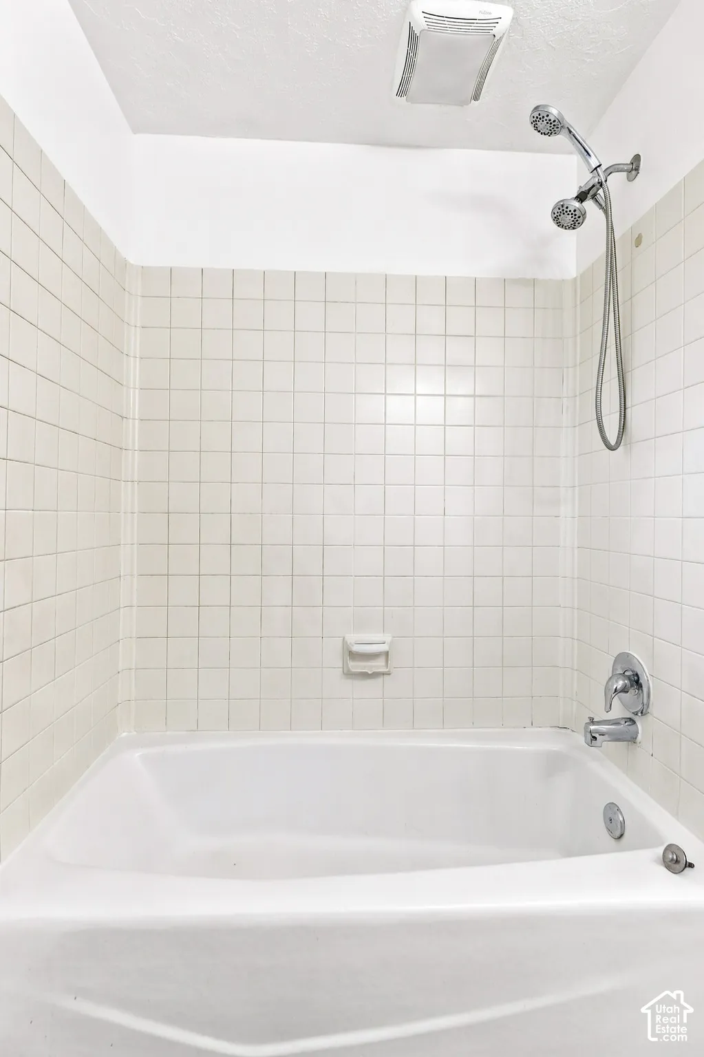Bathtub with white tile surround, chrome fixtures, and a ceiling-mounted ventilation unit