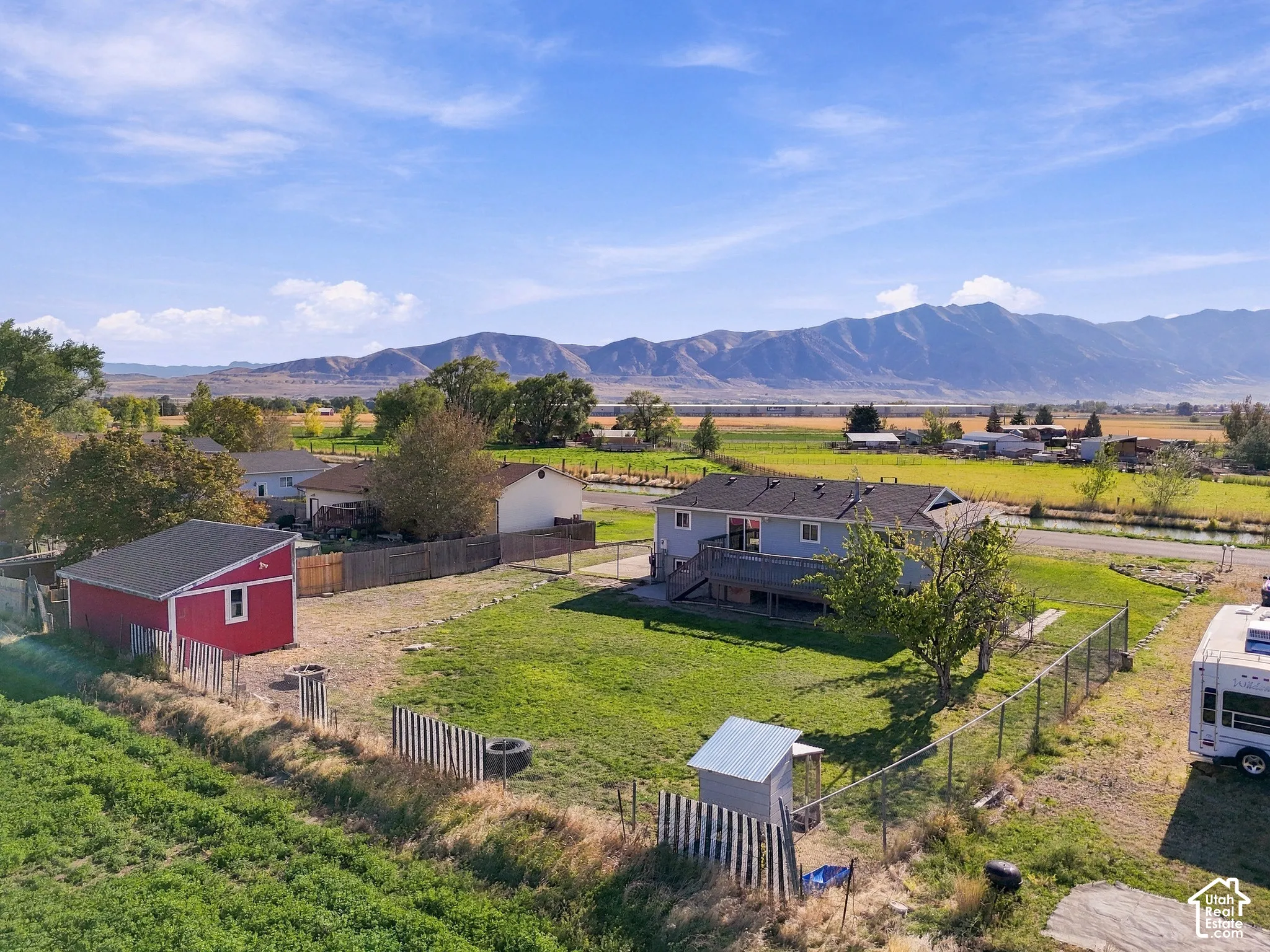 Expansive property featuring a detached red shed, chain-link fencing, a two-story residence with a deck, and distant mountain scenery