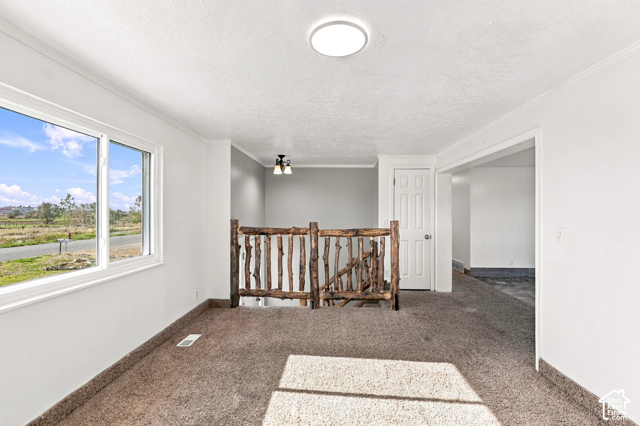Bright interior space featuring a window, wood railing, recessed ceiling light, and neutral carpeting