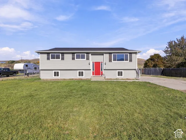 Split-level residence featuring light gray siding with a contrasting red entry door, a dark shingle roof, and a front yard with a green lawn