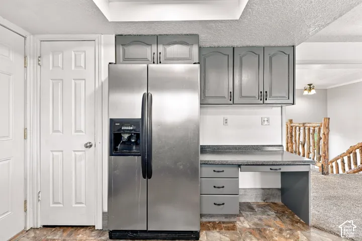 Stainless steel refrigerator, gray cabinetry, built-in desk, wood-finish flooring, and natural wood staircase railing
