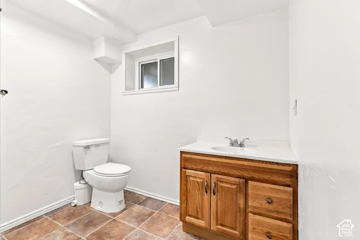Ceramic tile flooring, white toilet, single-pane window, wood-finish vanity with built-in sink, and a white countertop