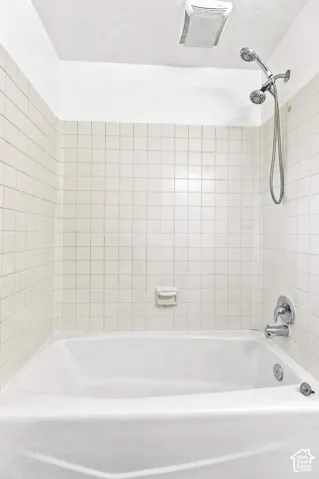 Bathtub with white tile surround, chrome fixtures, and a ceiling-mounted ventilation unit