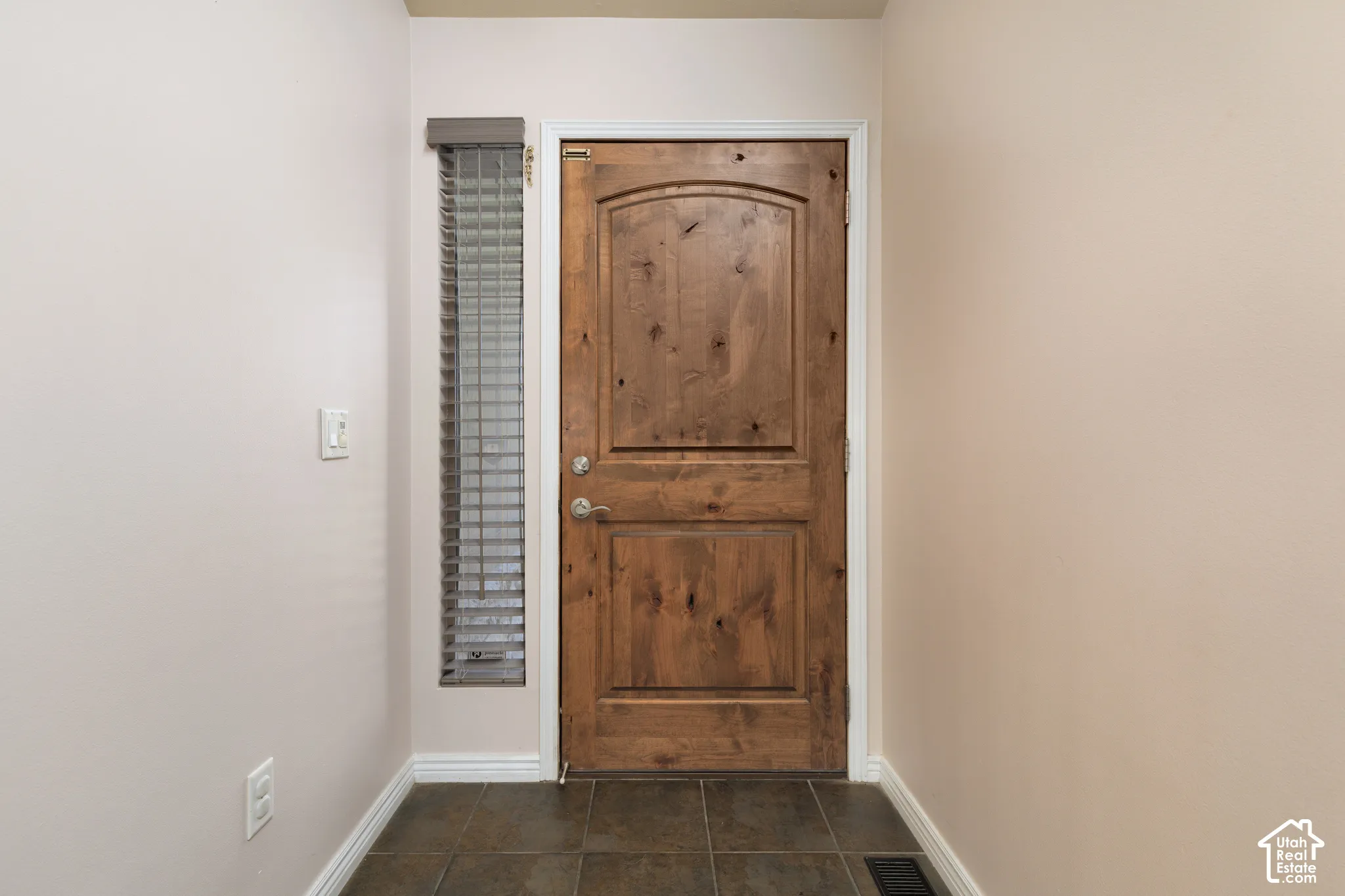 Arched wood door with a side window featuring blinds, tiled flooring, and light-toned wall finishes