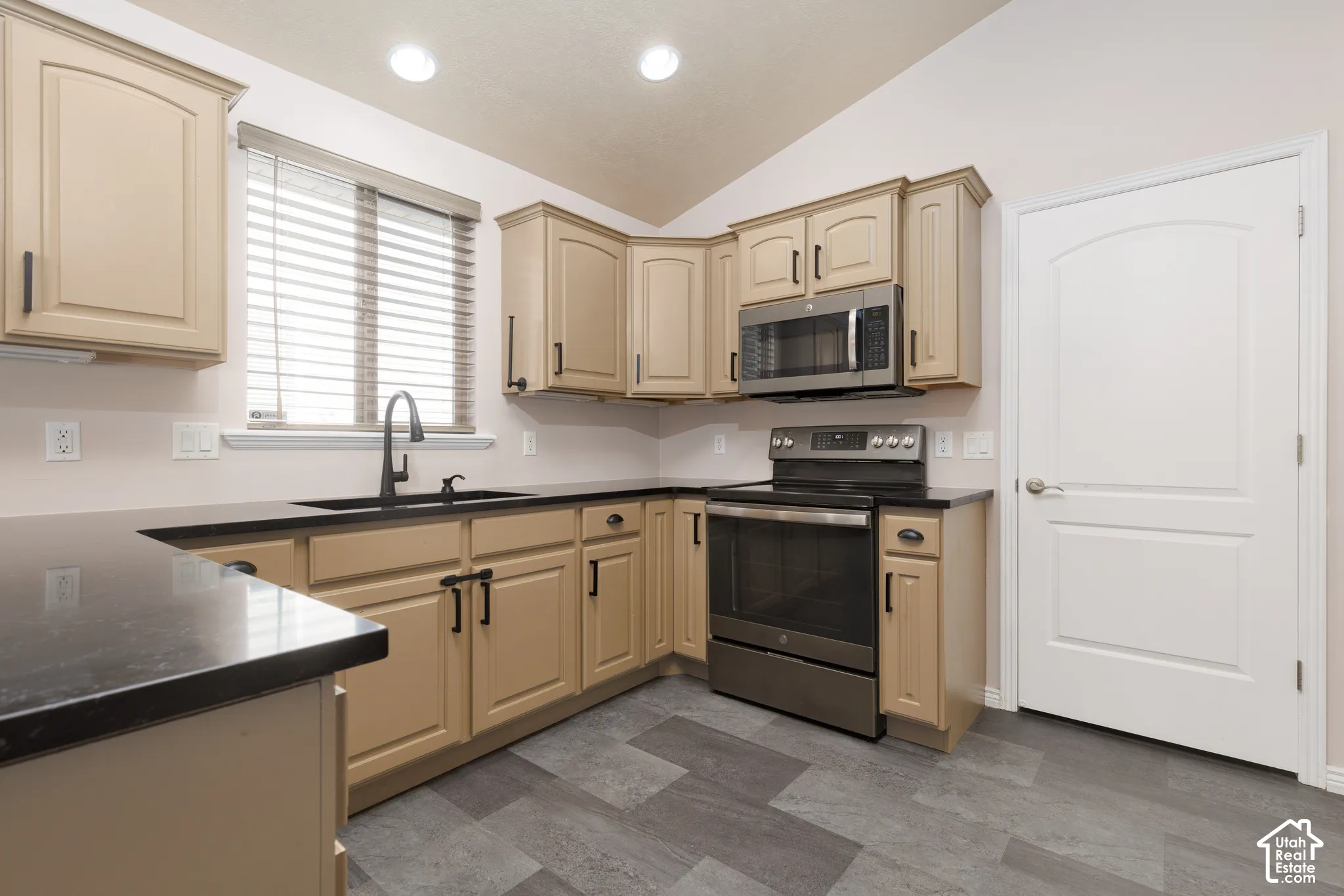 Kitchen featuring wood-finish cabinetry, dark countertops, stainless steel appliances, and a vaulted ceiling