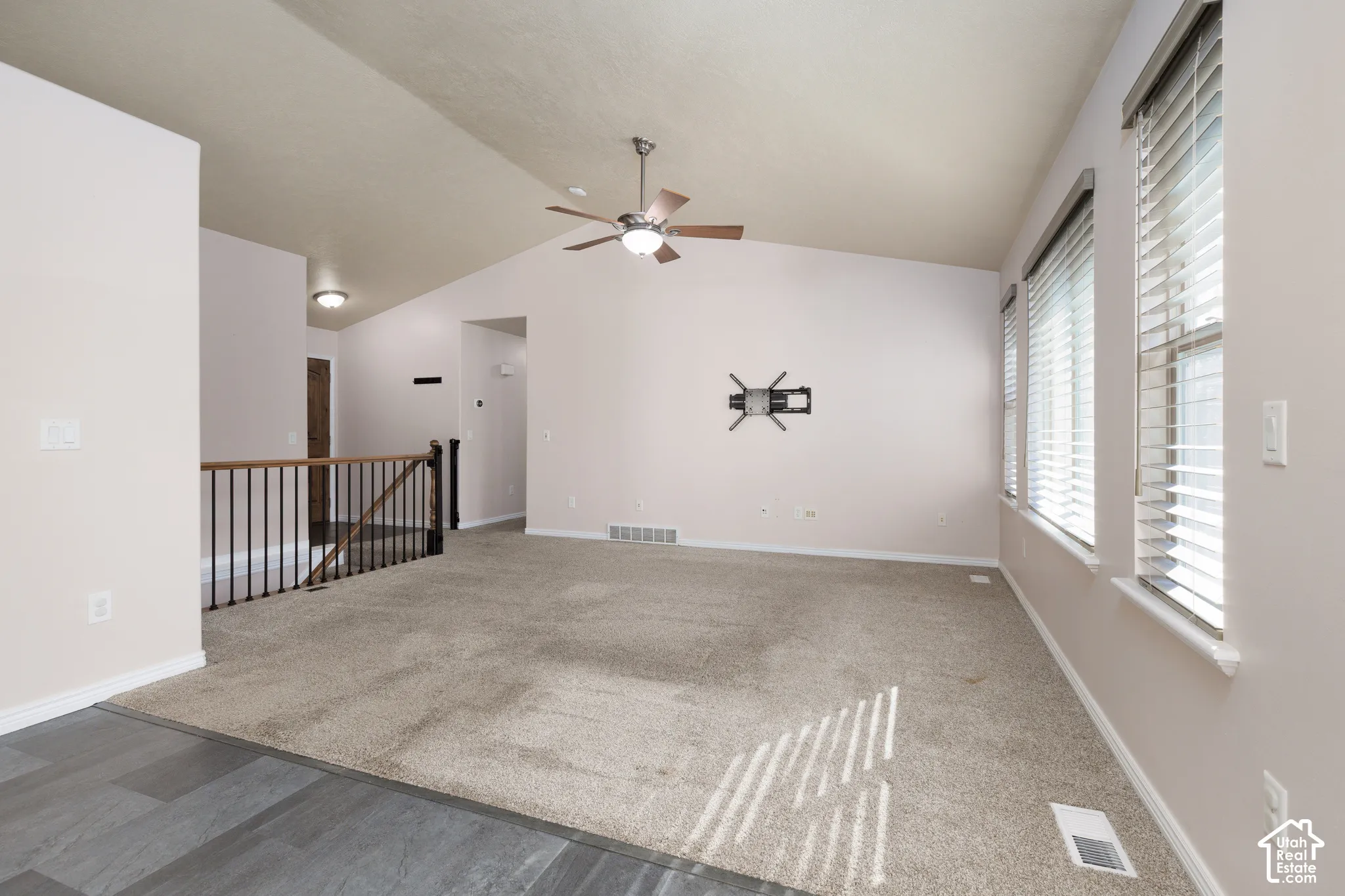 Vaulted ceiling with a ceiling fan, multiple windows with blinds, carpeted flooring, and a wood-finish flooring transition