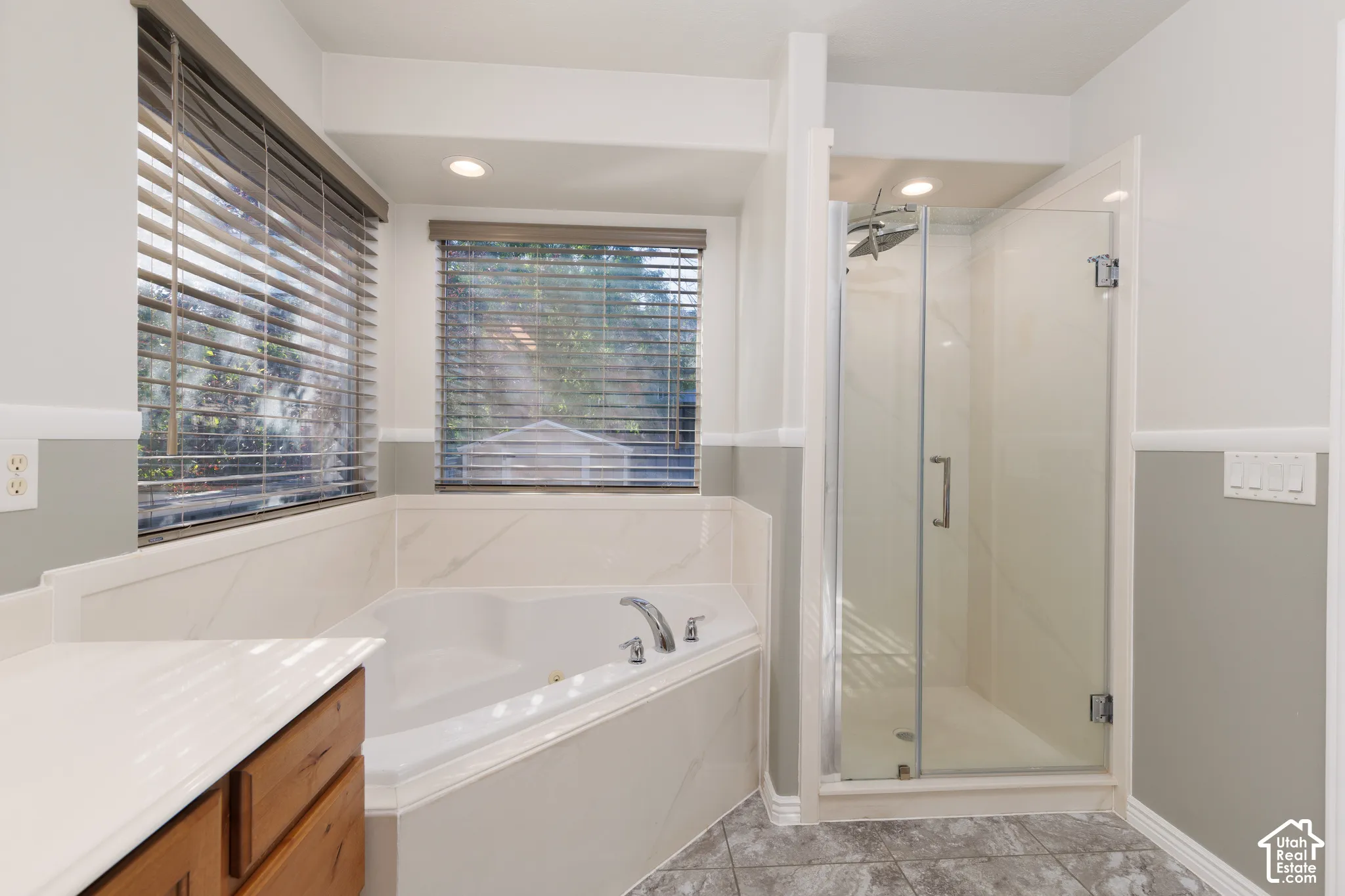 Built-in corner soaking tub with deck-mounted faucet, glass-enclosed shower, wood-finish cabinetry, and tiled flooring