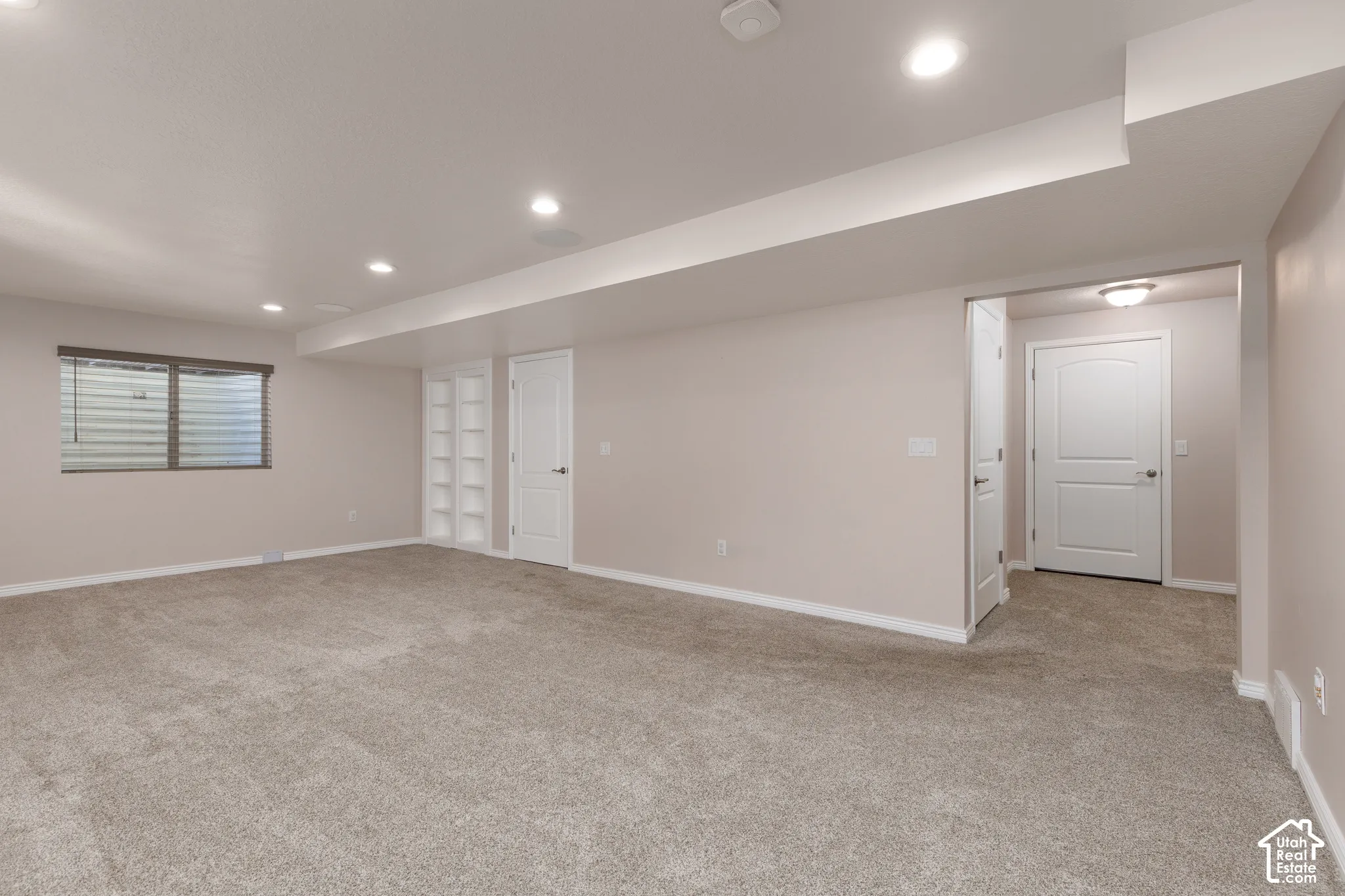 Spacious room featuring neutral carpeting, recessed lighting, a built-in shelving unit, and a window with blinds